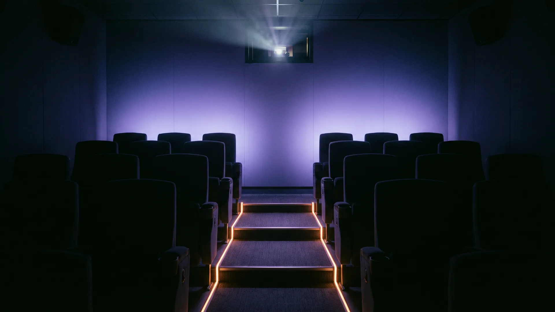 Rows of empty seats in a dark screening room, the screen lit violet.