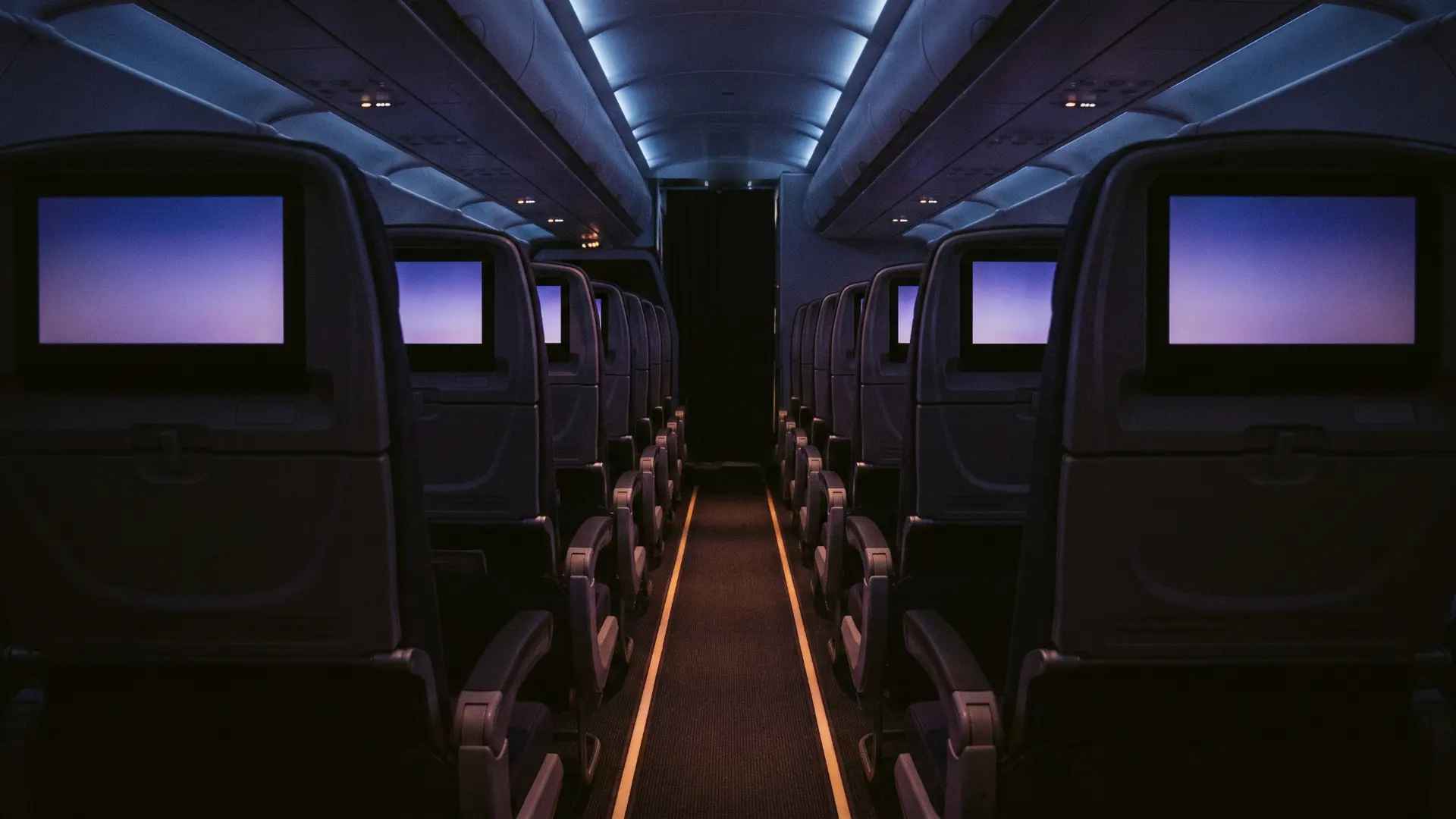 An empty aircraft cabin at night, every seatback screen glowing a soft violet.