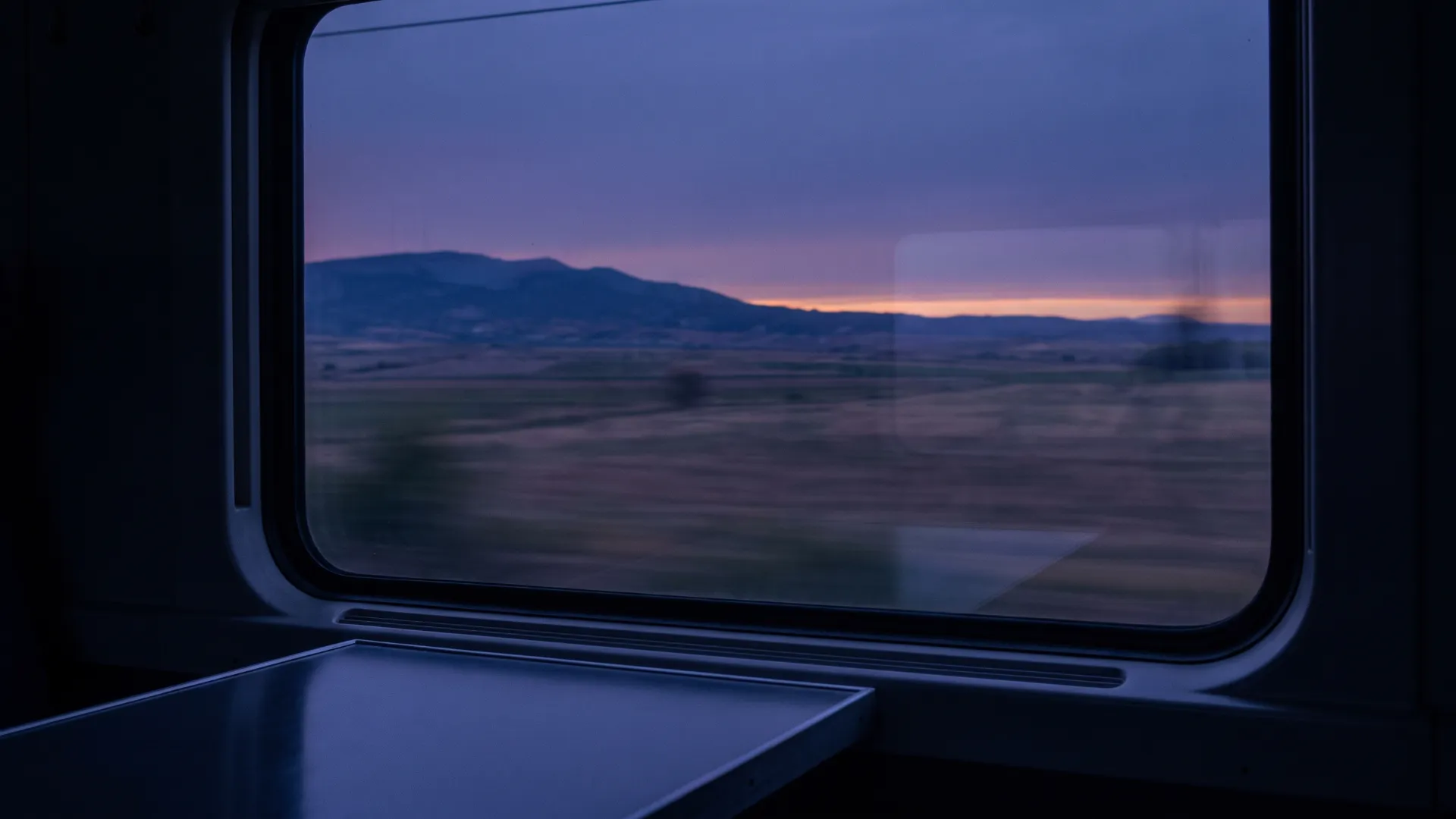An open landscape streaming past a train window at dusk.